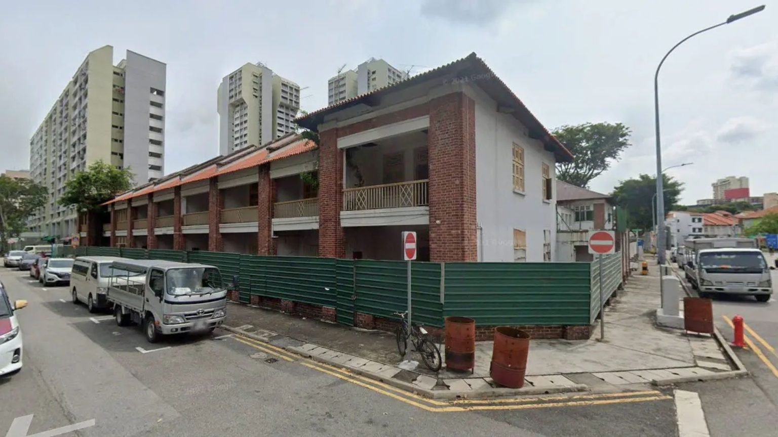 Two-storey conserved brick and white building under renovation near residential blocks with vehicles parked on the street