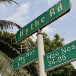 Green street signs for Hythe Road and house numbers 1-33 and 34-85 against a blue sky and palm leaves