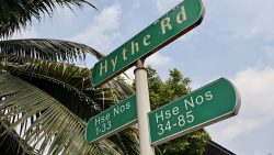 Green street signs for Hythe Road and house numbers 1-33 and 34-85 against a blue sky and palm leaves