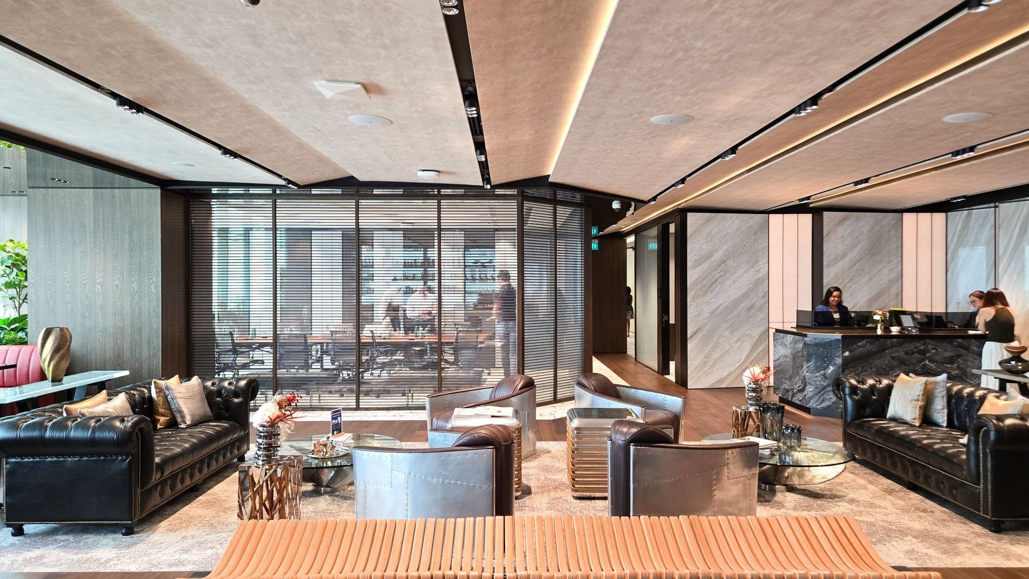 Residential lounge with leather sofas, metal armchairs, glass tables and a reception desk behind a glass partition