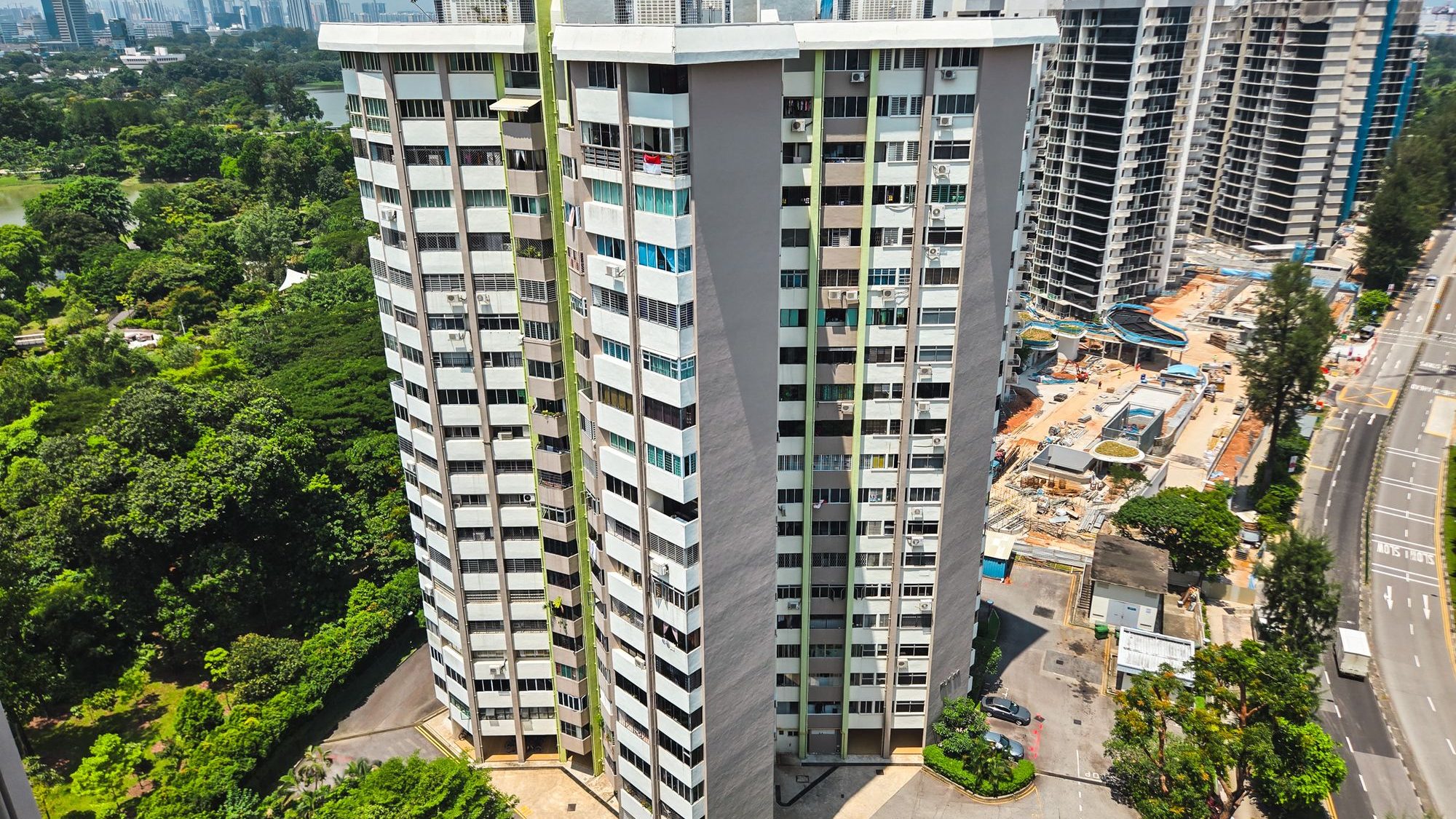 Two high-rise residential blocks near a large park and construction site along a road