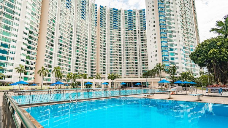 Costa Del Sol residential blocks surrounding an outdoor swimming pool with blue umbrellas and palm trees