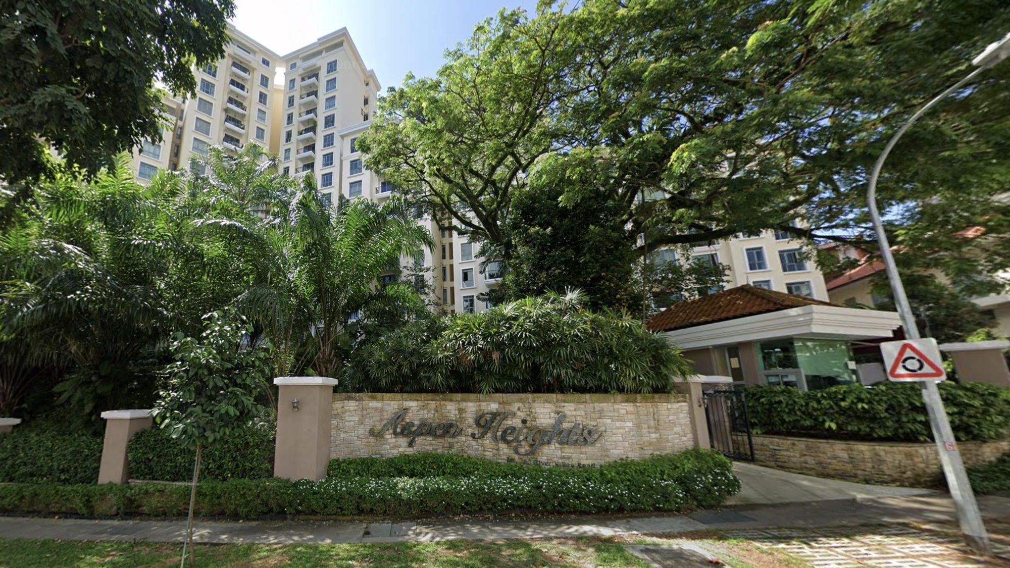 Aspen Heights apartment blocks behind lush greenery and a stone signboard at the entrance with gatehouse