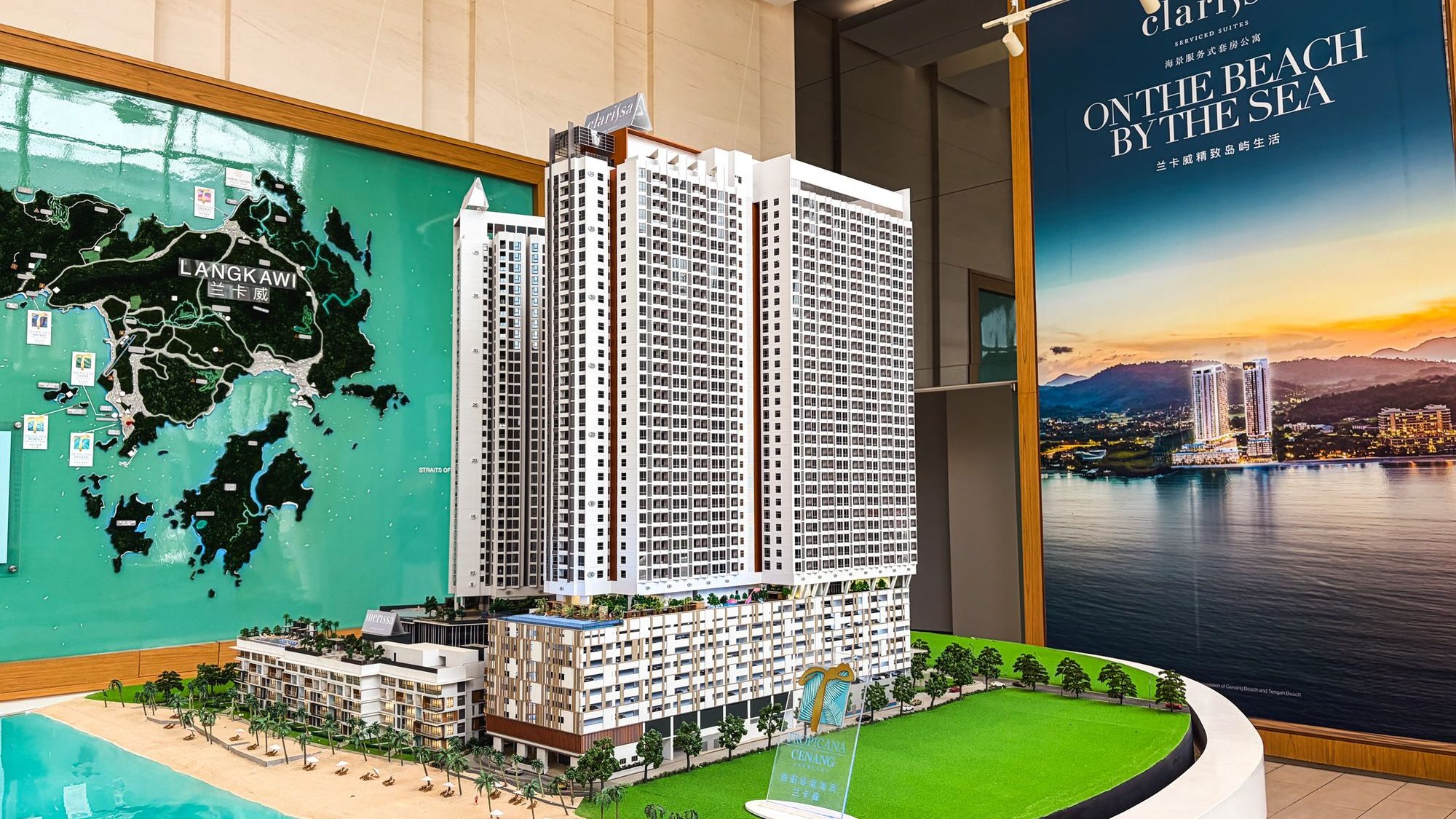 Scale model of a high-rise residential development with beach, greenery, map of Langkawi, and promotional poster