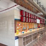Covered walkway with tiled floor, tiled wall, mural of kitchen utensils, red and white lanterns, stools and cubby shelves