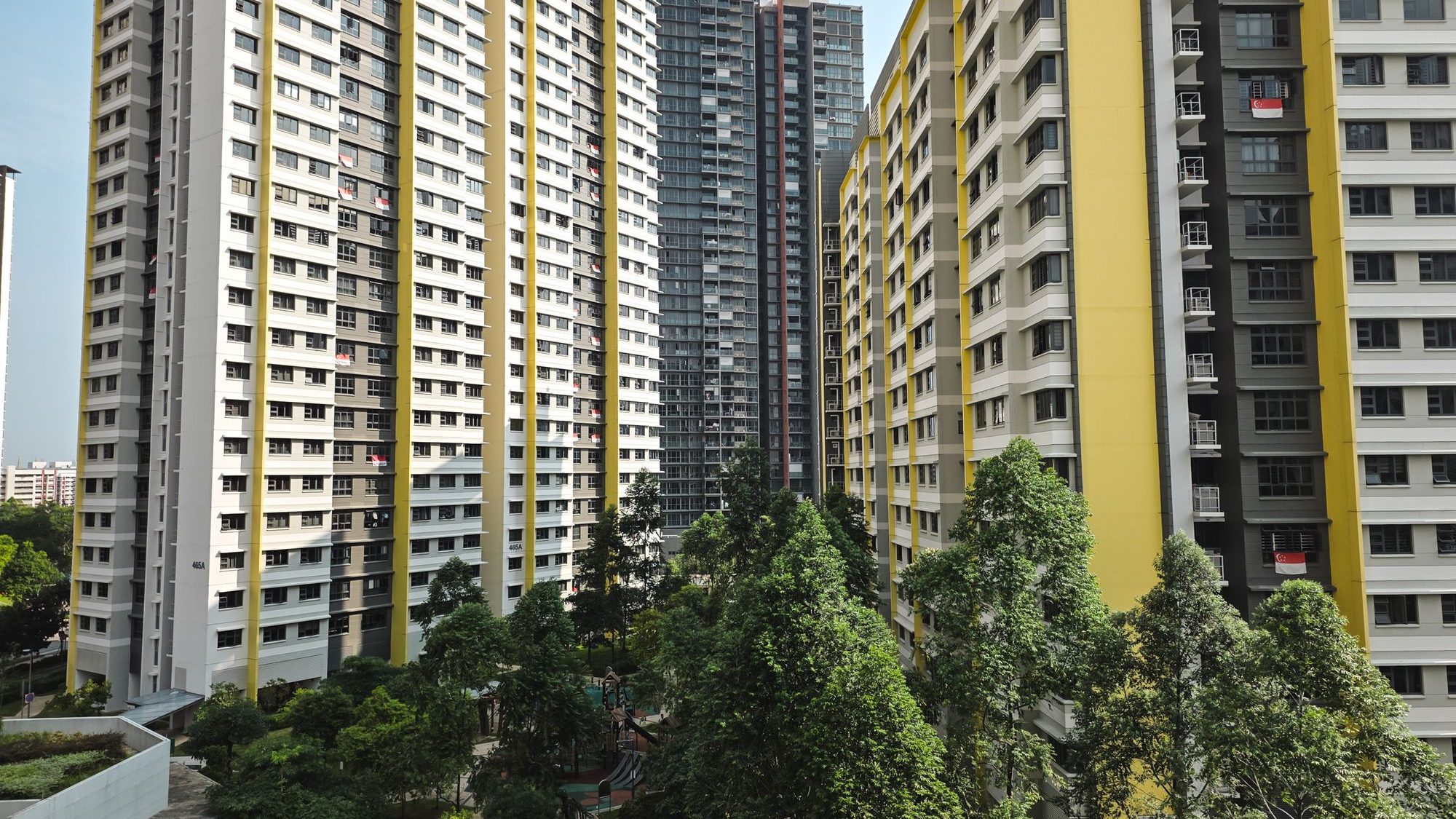 Housing blocks with Singapore flags hanging from some windows and green trees in the foreground
