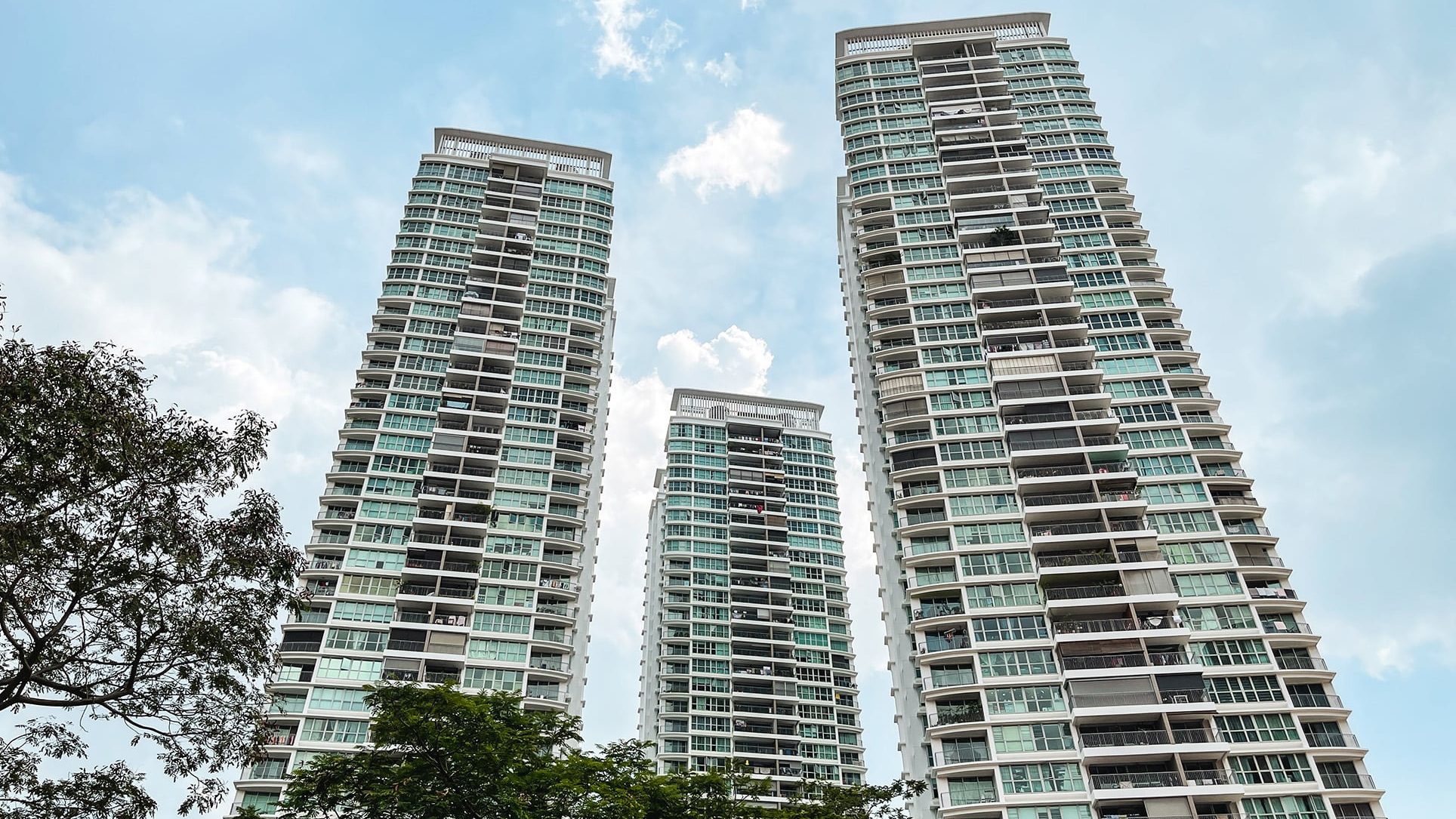 Natura Loft Bishan DBSS apartment blocks with balconies against a blue sky and trees in foreground