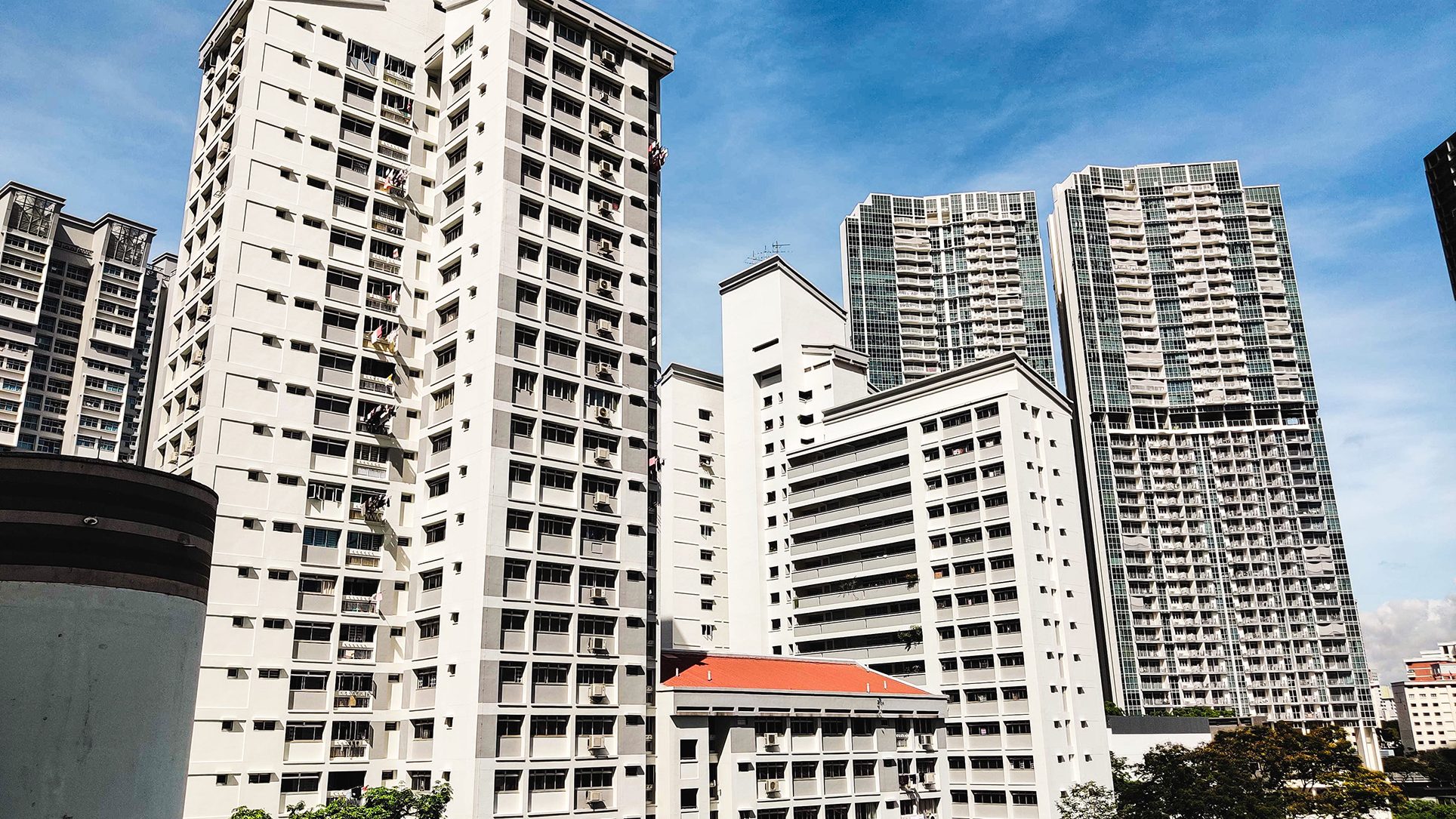 White HDB blocks with visible air conditioners and balconies against a blue sky with taller apartment blocks behind