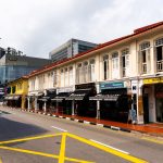 Shophouses with restaurants and clinics along a street with vehicles and modern buildings in the background