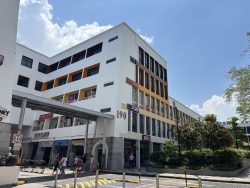Mid-rise commercial building with shops including KFC, Anytime Fitness, and remittance services under clear blue sky