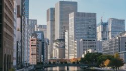 High-rise office buildings and a river with a tree-lined walkway in an urban area