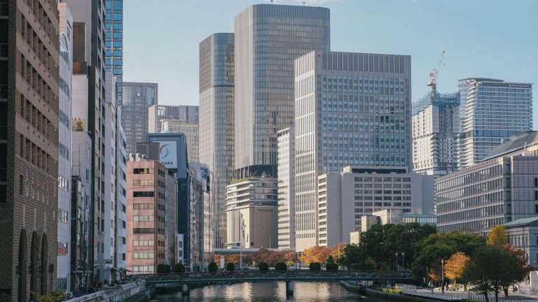 High-rise office buildings and a river with a tree-lined walkway in an urban area