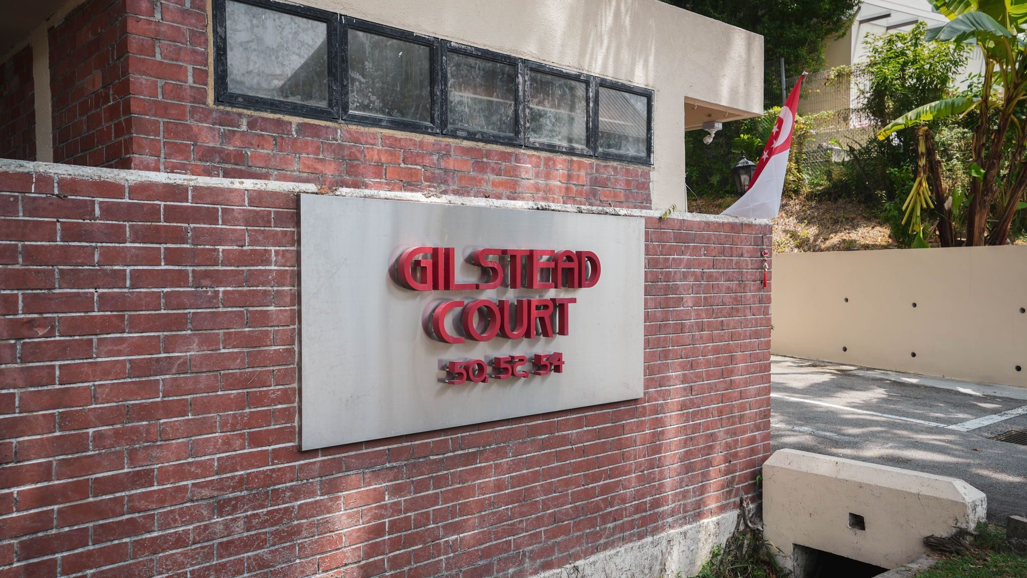 Gilstead Court sign with house numbers 50, 52, 54 on a brick wall near a gated driveway and Singapore flag