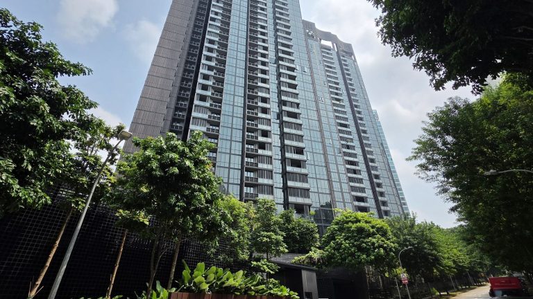 High-rise residential apartment blocks with glass balconies surrounded by lush green trees under a partly cloudy sky
