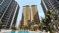 Residential towers surrounding a swimming pool with palm trees and a shaded seating area under a clear sky