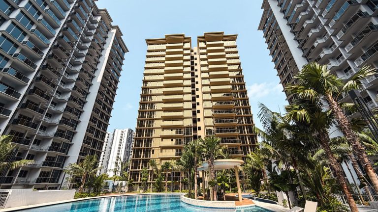 Residential towers surrounding a swimming pool with palm trees and a shaded seating area under a clear sky