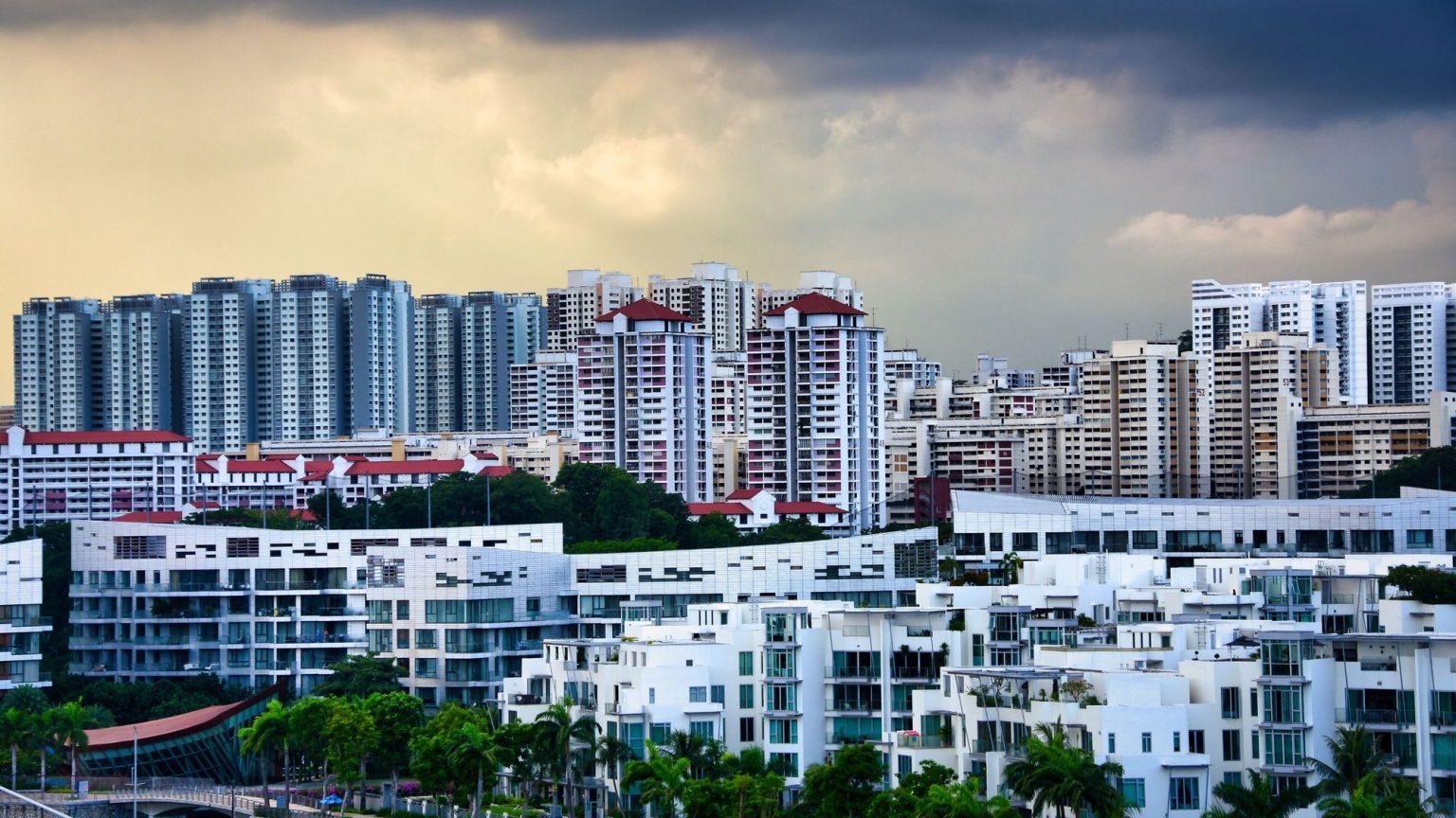Cluster of white low-rise apartments in front of taller residential blocks under cloudy sky