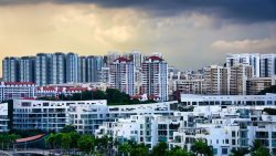 Cluster of white low-rise apartments in front of taller residential blocks under cloudy sky