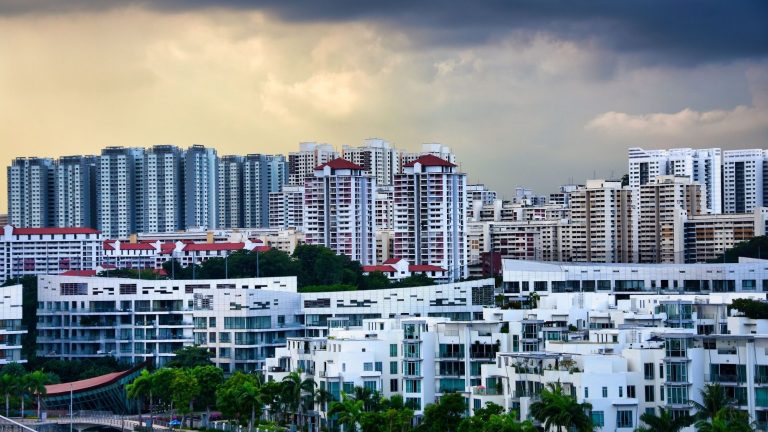 Cluster of white low-rise apartments in front of taller residential blocks under cloudy sky