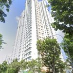 Tall white residential apartment blocks surrounded by lush green trees and blue sky