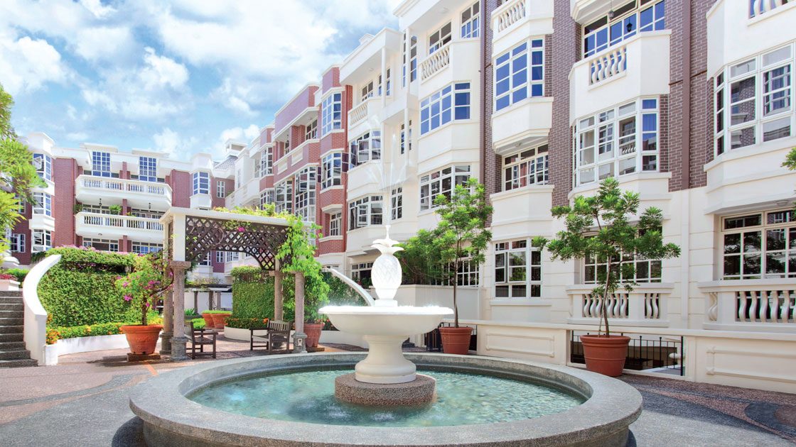 Fountain in front of low-rise residential blocks with white windows and balcony railings under blue sky