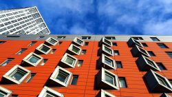 Residential block with orange cladding and protruding square windows beneath a blue sky