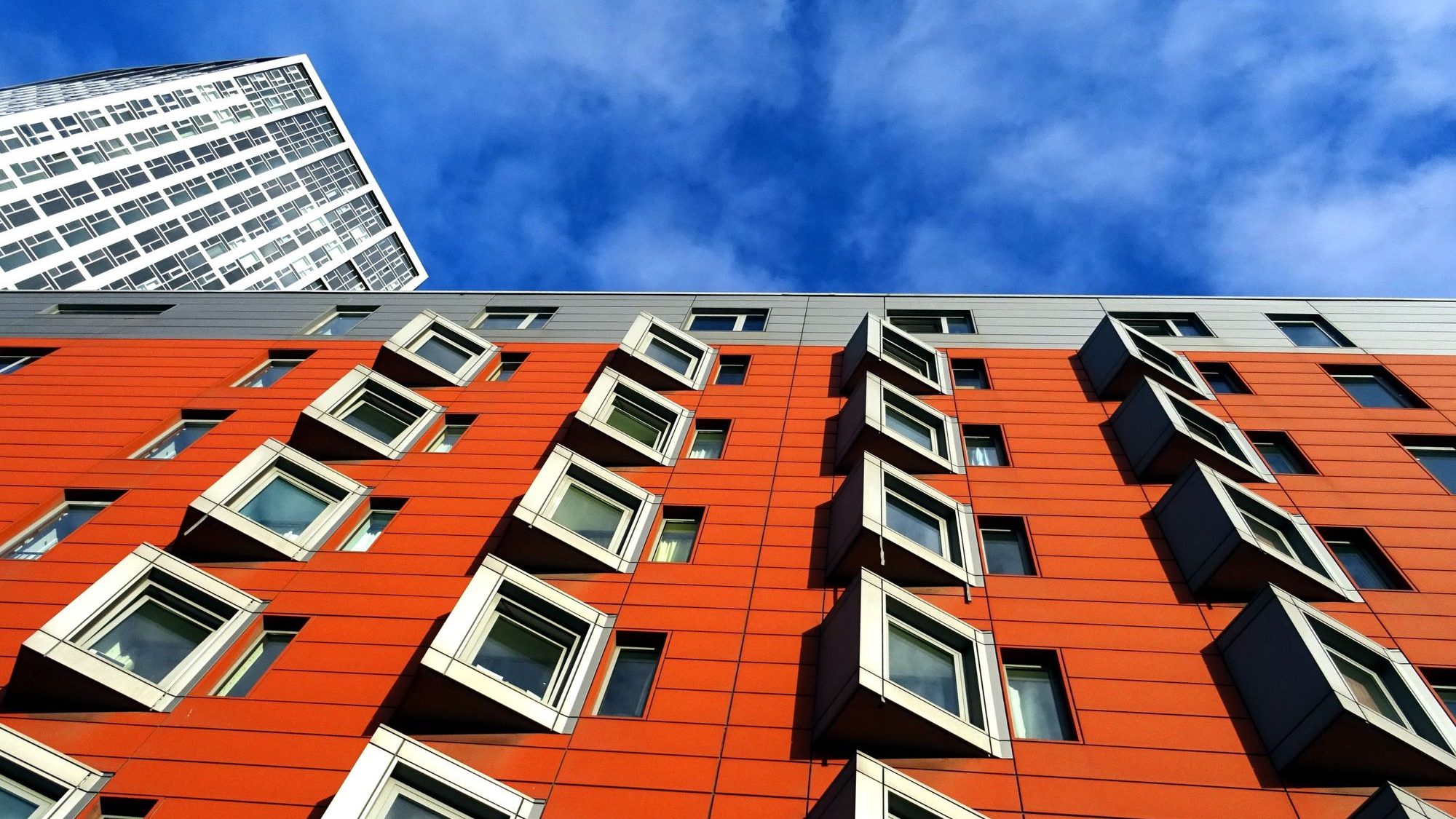 Residential block with orange cladding and protruding square windows beneath a blue sky