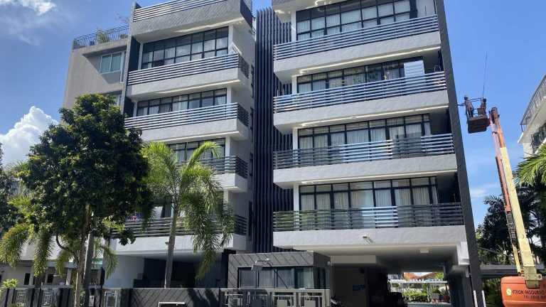 Mid-rise residential apartment blocks with balconies, surrounded by palm trees and a worker on a lift cleaning the building facade