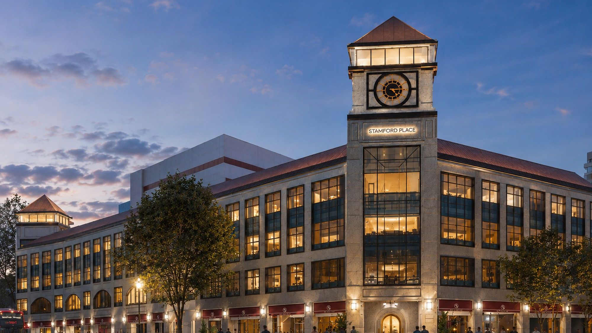 Stamford Place office and retail building with clock tower lit at dusk and people walking below