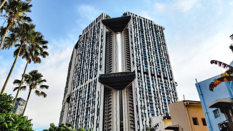 Tall residential building with balconies and unique elevated sky gardens in an urban area with palm trees