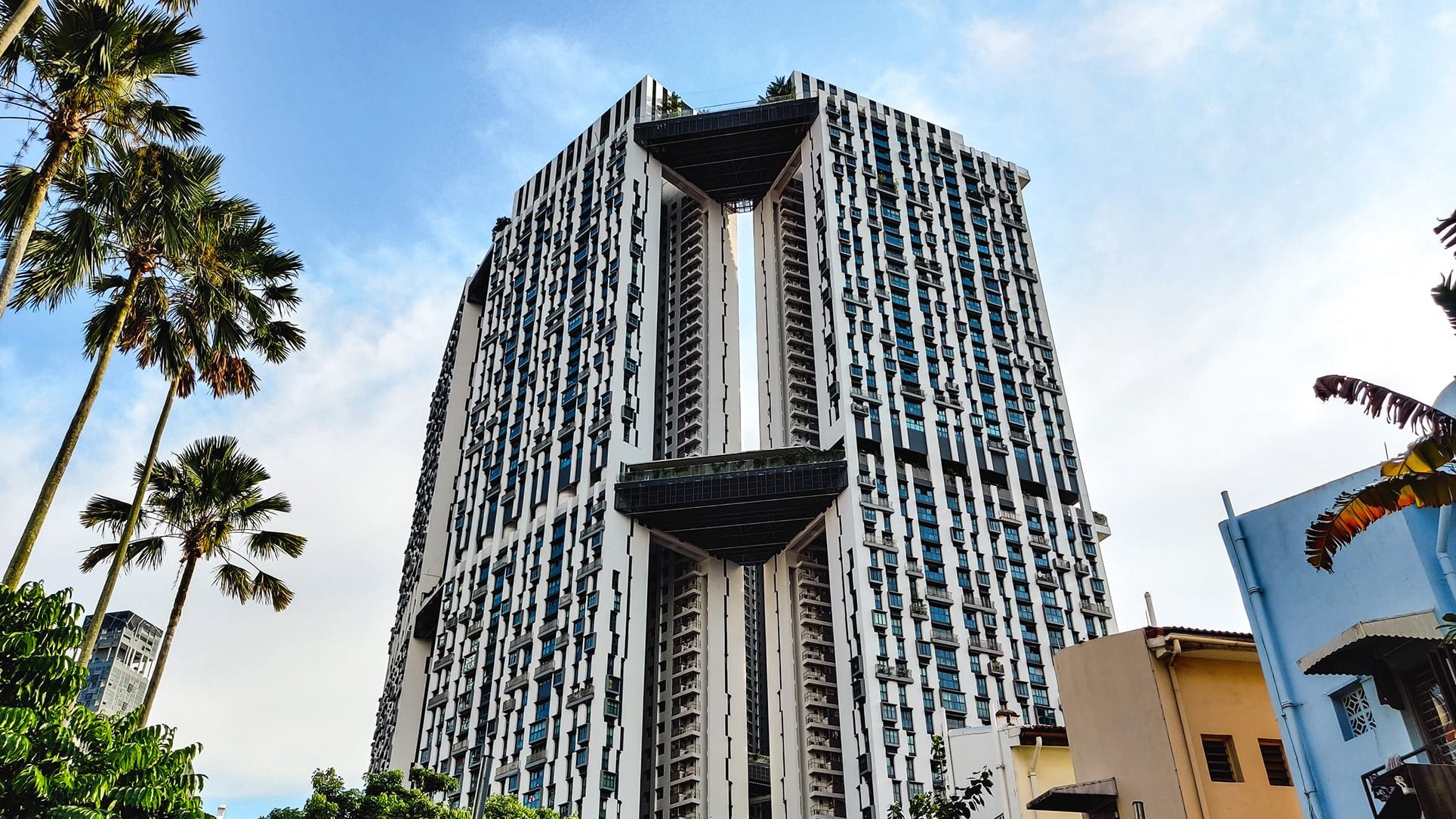Tall residential building with balconies and unique elevated sky gardens in an urban area with palm trees