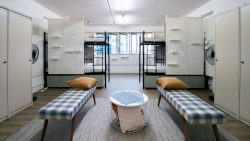 Room with two sets of metal bunk beds, plaid benches with brown pillows and lockers along the walls