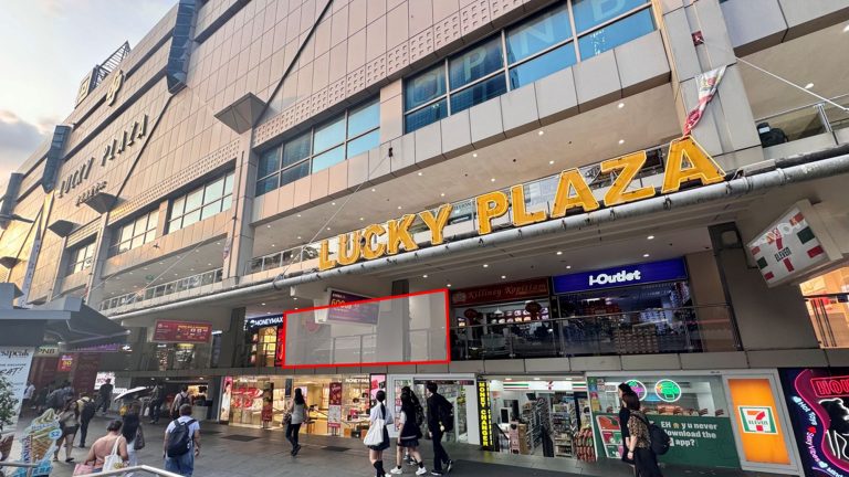 Lucky Plaza shopping mall facade with people walking and various shop signs including 7-Eleven and i-Outlet