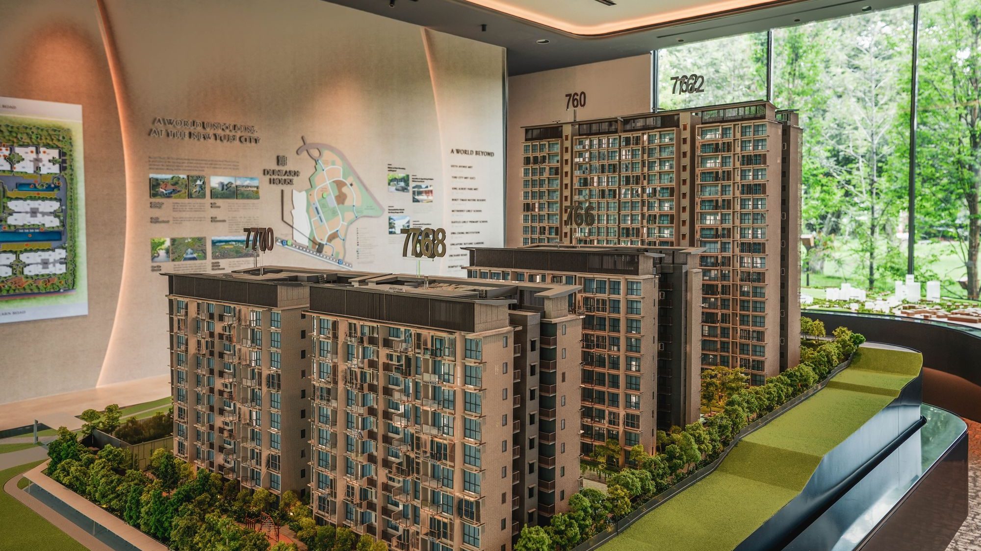 Scale model of residential apartment blocks with detailed greenery and layout maps in the background