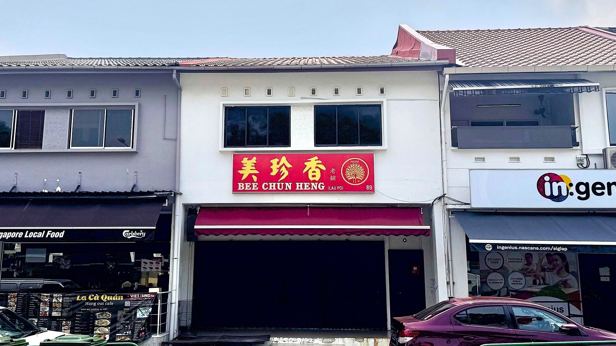 Two-storey shop houses with retail signs for Bee Chun Heng and Ingenius, and a maroon car parked outside