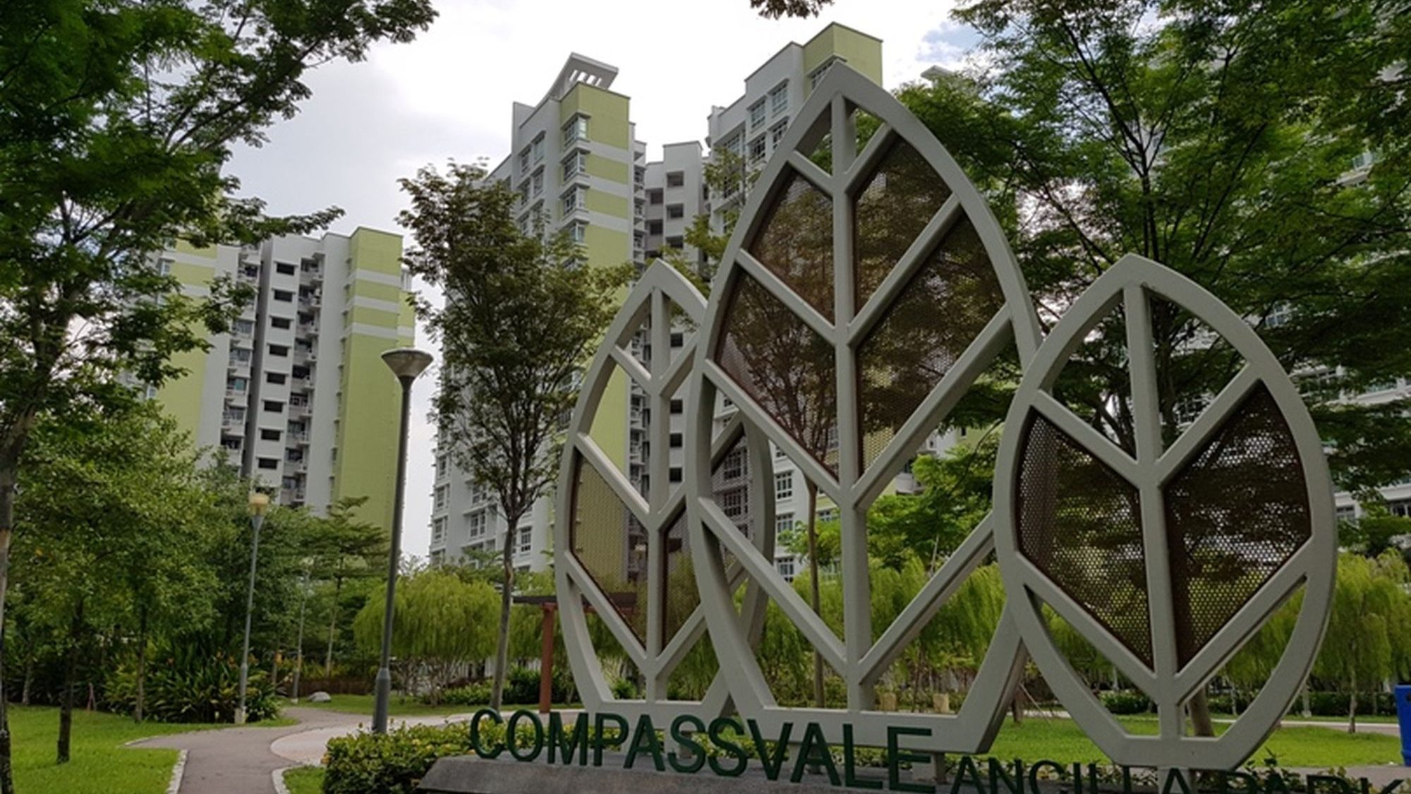Compassvale Ancilla residential blocks with leaf-shaped metal structures and surrounding trees in the foreground