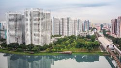 High-rise residential blocks near a body of water with greenery and an MRT station on the right side