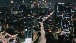 Tall residential and office buildings along lit roads with distant city skyline at night