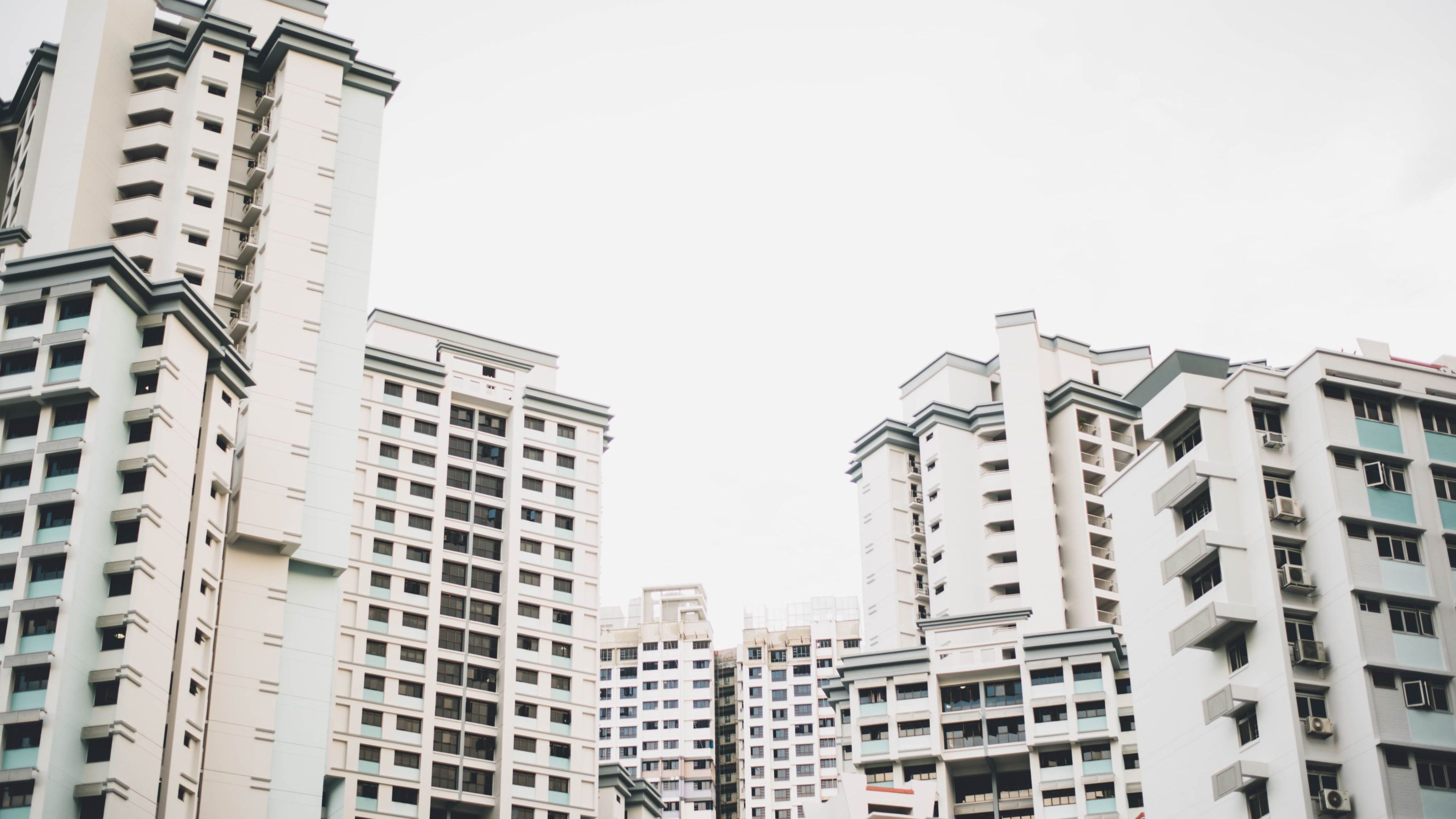 Tall white residential apartment blocks with balconies and air-conditioning units under an overcast sky
