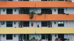 Housing block with orange and yellow corridors, plants on balconies, and people walking and drying clothes