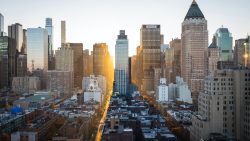 City skyline with tall buildings and sunlight shining down a street between them