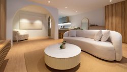 Living room with curved white sofa, round marble coffee table, wood panel wall and kitchen in background