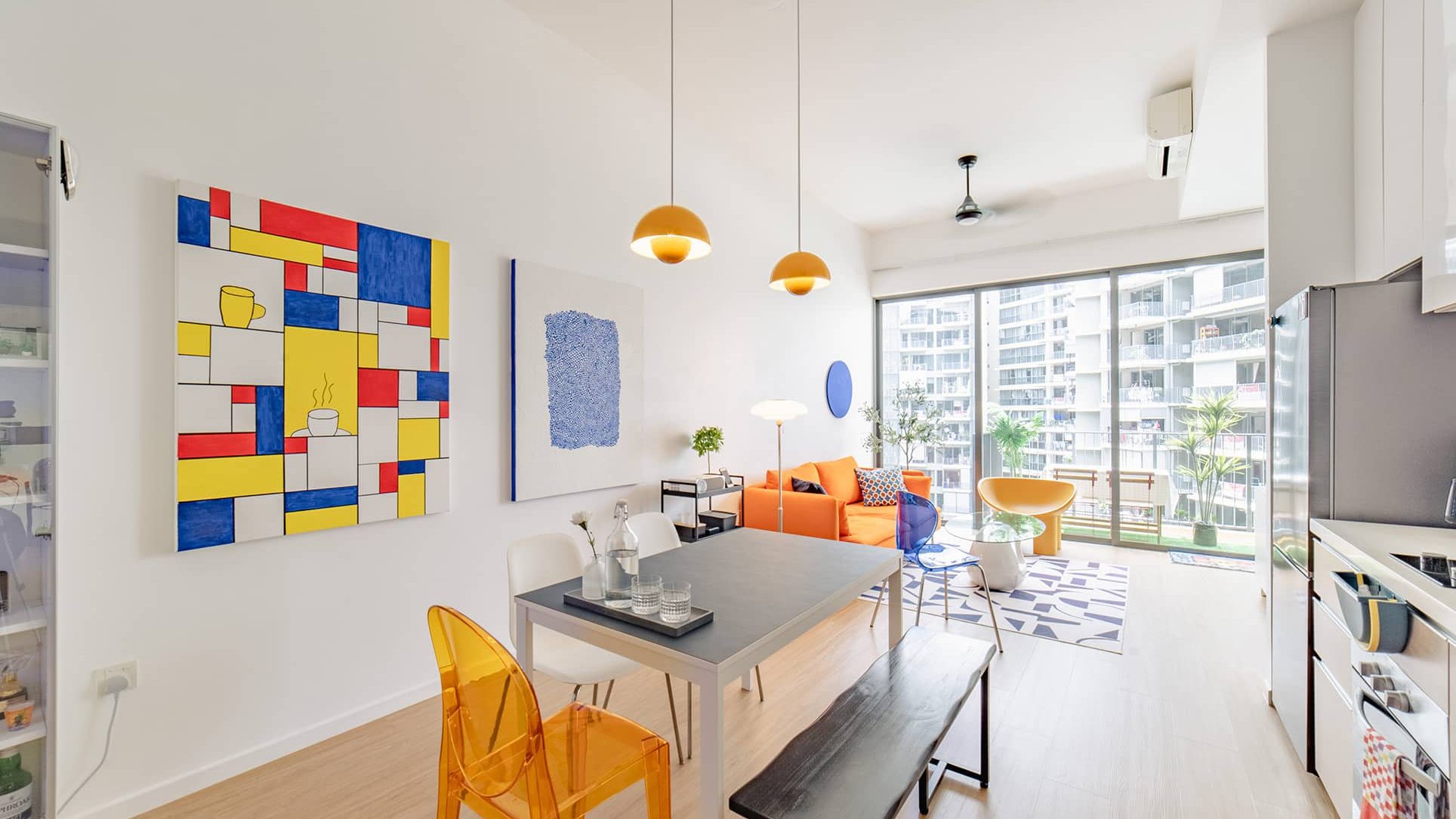 Dining table with mixed chairs beside an orange sofa and glass sliding doors in a living room
