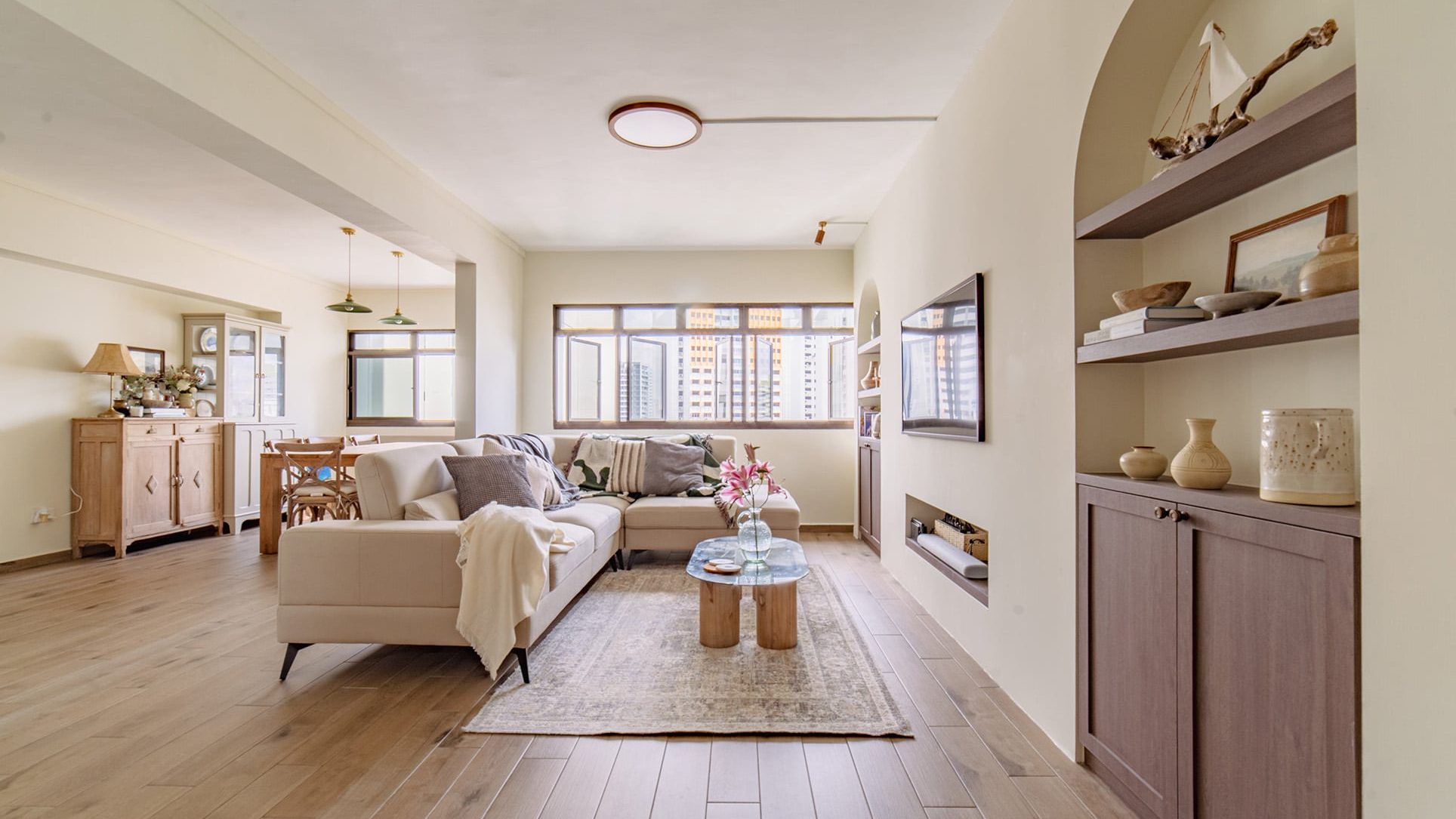 Living room with beige sectional sofa, wooden coffee table, built-in shelves, and dining area behind