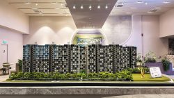 Tenet EC scale model with multiple apartment blocks, trees, and a site map in a showroom setting