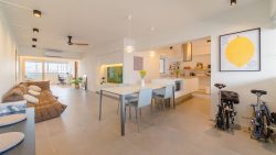 Open-plan living and dining area with brown sofa, dining table, kitchen island, and bicycles near lemon artwork