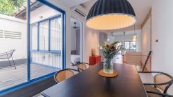 Dining area with black table, cane chairs, hanging lamp, flower vase, and sliding glass door to patio with chair