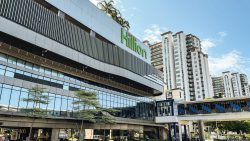Hillion shopping mall with glass facade and trees outside, beside tall white residential apartment blocks