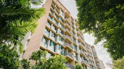 Residential apartment building with balconies framed by lush green trees under a cloudy sky