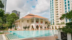 Swimming pool in front of a colonial-style clubhouse with high-rise residential blocks and greenery surrounding it